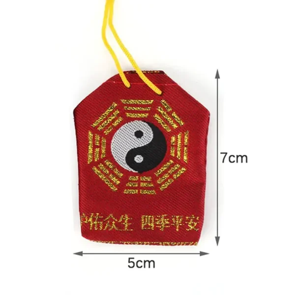 mage d'une petite pochette d'amulette yin yang en tissu rouge, mesurant 7 cm de hauteur et 5 cm de largeur, suspendue par un cordon jaune. Au centre, le symbole Yin Yang en noir et blanc est encadré par des caractères chinois dorés. Les dimensions de l'amulette sont clairement indiquées sur l'image, illustrant sa taille compacte et portable.